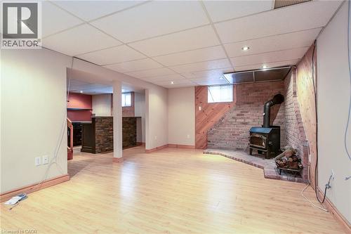 Unfurnished living room featuring a paneled ceiling, wooden walls, a wood stove, and light wood finished floors - 120 Fourth Avenue, Kitchener, ON 