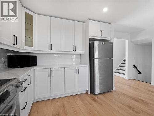 Kitchen with stove, backsplash, light wood-style floors, freestanding refrigerator, and white cabinets - 24 Keefer Road, Thorold, ON - Indoor Photo Showing Kitchen