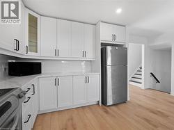 Kitchen with stove, backsplash, light wood-style floors, freestanding refrigerator, and white cabinets - 