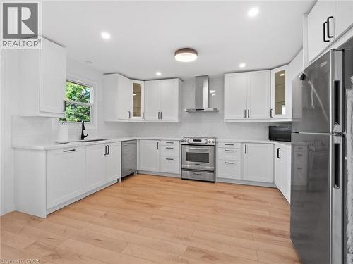 Kitchen featuring light wood-style floors, wall chimney range hood, stainless steel appliances, and backsplash - 24 Keefer Road, Thorold, ON - Indoor Photo Showing Kitchen With Upgraded Kitchen