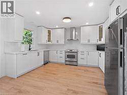 Kitchen featuring light wood-style floors, wall chimney range hood, stainless steel appliances, and backsplash - 
