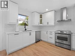 Kitchen with light countertops, a sink, stainless steel range with electric cooktop, light wood finished floors, and wall chimney range hood - 