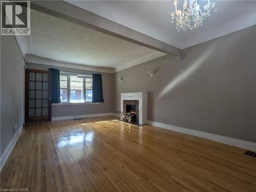 Unfurnished living room with a brick fireplace, beam ceiling, wood-type flooring, and a chandelier - 59 Dunkirk Drive, Hamilton, ON - Indoor With Fireplace