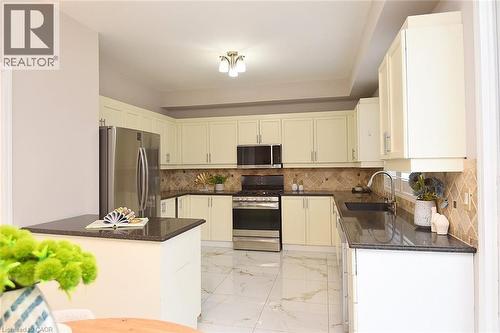 Kitchen featuring stainless steel appliances, light marble finish flooring, dark stone counters, and tasteful backsplash - 5109 Blue Spruce Avenue, Burlington, ON - Indoor Photo Showing Kitchen