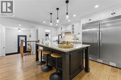 Kitchen with stainless steel built in refrigerator, glass insert cabinets, light stone countertops, white cabinetry, and a breakfast bar - 
