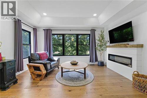 Living area with a tray ceiling, a glass covered fireplace, light wood-style floors, plenty of natural light, and recessed lighting - 115 Lakeshore Road, Port Burwell, ON - Indoor Photo Showing Living Room With Fireplace