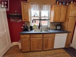 The kitchen features natural wood cabinetry, a double gooseneck sink framed by a wide window view, and access to the semi-refinished mudroom. Appliances included: fridge, stove, range hood, microwave, - 