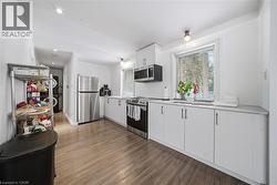 Kitchen featuring white cabinetry, stainless steel appliances, light countertops, and dark wood finished floors - 