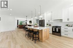Kitchen with appliances with stainless steel finishes, a kitchen island, white cabinets, a breakfast bar area, and hanging light fixtures - 