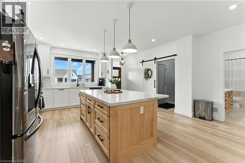 Kitchen featuring a barn door, stainless steel refrigerator with ice dispenser, light stone counters, white cabinets, and a center island - 9 Macneil Court, Port Burwell, ON - Indoor Photo Showing Kitchen With Upgraded Kitchen