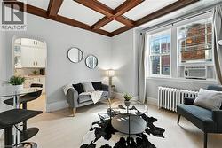 Living room with coffered ceiling, radiator, beamed ceiling, light wood-style flooring, and arched walkways - 
