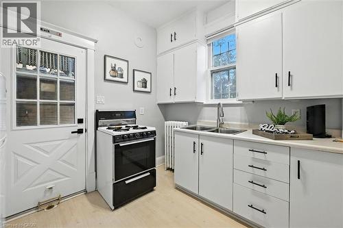 Kitchen featuring light countertops, white cabinetry, gas range oven, radiator, and light wood-style flooring - 1047 Main Street E, Hamilton, ON - Indoor Photo Showing Kitchen With Double Sink