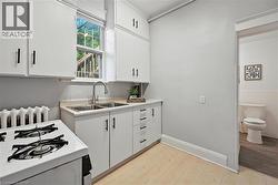 Kitchen with white range with gas cooktop, light countertops, white cabinets, light wood-style floors, and radiator - 