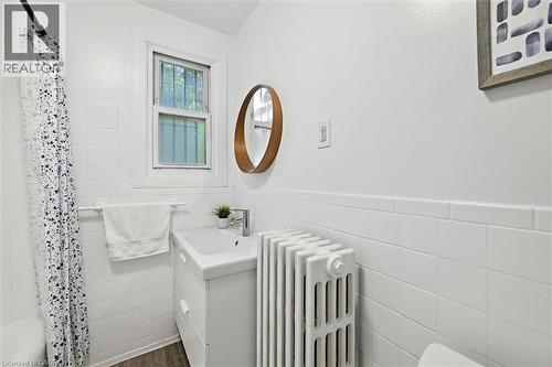 Full bathroom featuring wainscoting, radiator heating unit, tile walls, vanity, and dark wood-type flooring - 1047 Main Street E, Hamilton, ON - Indoor Photo Showing Bathroom