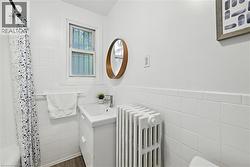 Full bathroom featuring wainscoting, radiator heating unit, tile walls, vanity, and dark wood-type flooring - 
