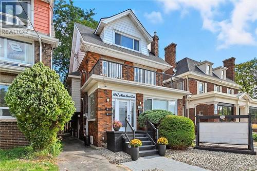 View of front facade featuring brick siding, a balcony, and a shingled roof - 1047 Main Street E, Hamilton, ON - Outdoor With Facade