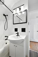 Full bath with tile walls, vanity,  shower combination, dark wood-style floors, and wainscoting - 