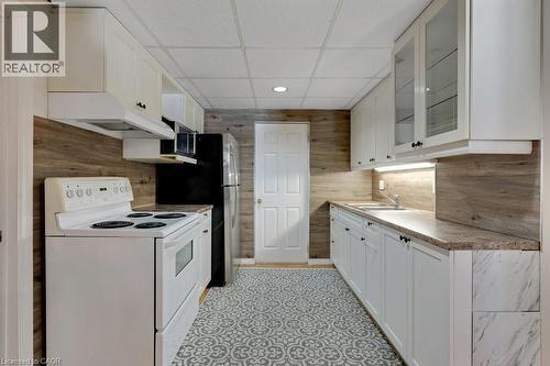 Lower Kitchen featuring electric range, a paneled ceiling, white cabinets, light countertops, and glass fronted cabinets - 148 Cowan Boulevard, Cambridge, ON - Indoor Photo Showing Kitchen