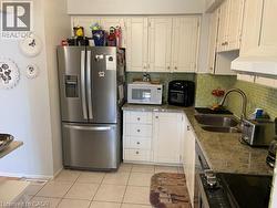 Kitchen featuring stainless steel fridge, white microwave, a sink, white cabinetry, and decorative backsplash - 