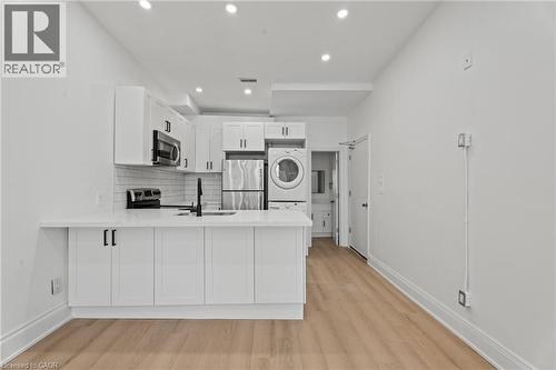 Kitchen featuring white cabinetry, a peninsula, backsplash, stainless steel appliances, and light wood-style floors - 93 John Street S, Hamilton, ON 