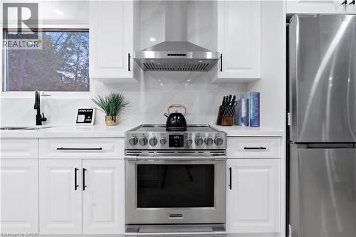 Kitchen featuring appliances with stainless steel finishes, wall chimney exhaust hood, white cabinetry, light stone countertops, and backsplash - 19 Broad Street, Brantford, ON - Indoor Photo Showing Kitchen With Stainless Steel Kitchen With Upgraded Kitchen