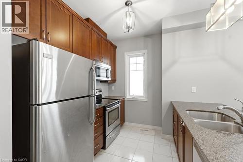 Kitchen featuring dark stone counters, stainless steel appliances, wood finish cabinetry, and light tile patterned flooring - 4 Andruss Lane, Ancaster, ON - Indoor Photo Showing Kitchen With Stainless Steel Kitchen With Double Sink