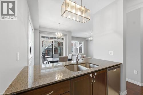 Kitchen with light stone counters, stainless steel dishwasher, a chandelier, dark wood finish cabinetry, and dark wood-style floors - 4 Andruss Lane, Ancaster, ON - Indoor Photo Showing Kitchen With Double Sink