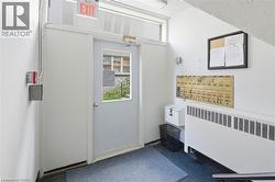 Entryway featuring a white door with a window pane, an overhead ""EXIT"" sign, a wall-mounted mailbox system, and a baseboard heating unit - 