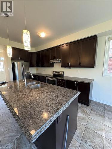Kitchen featuring dark brown cabinets, refrigerator, stainless steel range with electric cooktop, dark stone countertops, and decorative light fixtures - 50 Shoreacres Drive, Kitchener, ON - Indoor Photo Showing Kitchen With Double Sink