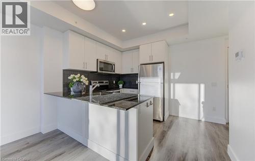 Kitchen with dark stone countertops, stainless steel appliances, white cabinetry, light wood-style flooring, and a peninsula - 103 Roger Street Unit# 310, Waterloo, ON - Indoor Photo Showing Kitchen With Stainless Steel Kitchen