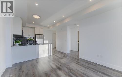 Kitchen with white cabinets, stainless steel appliances, light wood-type flooring, dark stone counters, and open floor plan - 103 Roger Street Unit# 310, Waterloo, ON - Indoor Photo Showing Kitchen
