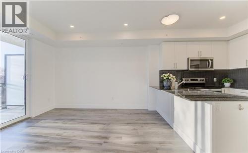 Kitchen featuring dark stone counters, white cabinets, stainless steel appliances, light wood-type flooring, and tasteful backsplash - 103 Roger Street Unit# 310, Waterloo, ON - Indoor Photo Showing Kitchen