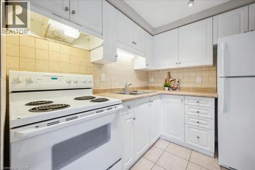 Kitchen with white appliances, under cabinet range hood, light countertops, white cabinets, and light tile patterned floors - 66 Rodgers Road Unit# 2, Guelph, ON - Indoor Photo Showing Kitchen With Double Sink