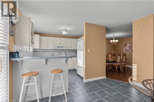 Kitchen with a kitchen bar, dark tile patterned flooring, a peninsula, white appliances, and tasteful backsplash - 42 Archer Way, Hamilton, ON - Indoor Photo Showing Kitchen