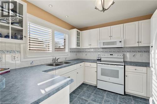 Kitchen featuring glass fronted cabinets, white appliances, dark countertops, and white cabinets - 42 Archer Way, Hamilton, ON - Indoor Photo Showing Kitchen With Double Sink
