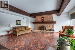 Living area with a textured ceiling, beam ceiling, brick patterned flooring, and a brick fireplace - 