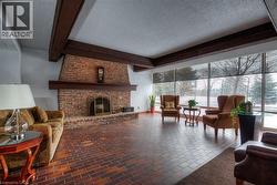 Living room featuring a textured ceiling, beam ceiling, a fireplace, and brick floors - 