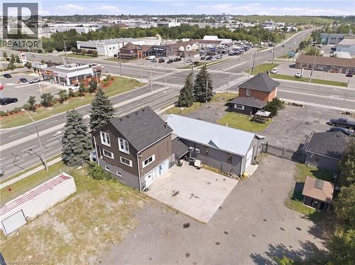 Aerial overview of a multi-structure property featuring a main building with dark siding and white-framed windows, an attached commercial-style building with a metal roof and garage door, and a separa - 1360 Rymal Road E, Hamilton, ON 