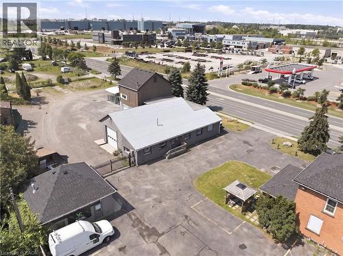 Industrial property featuring a main building with a metal roof and large garage door, a secondary building with a dark shingle roof, ample paved and gravel lot space, and mature evergreen trees - 1360 Rymal Road E, Hamilton, ON 