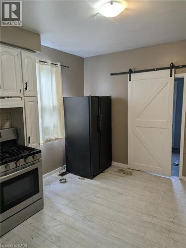 Kitchen featuring stainless steel range with gas cooktop, a barn door, black refrigerator with ice dispenser, light wood-type flooring, and white cabinetry - 151 Gibson Avenue, Hamilton, ON - Indoor Photo Showing Kitchen