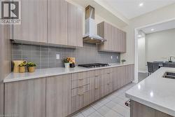 Kitchen with modern cabinets, light stone counters, wall chimney range hood, light brown cabinets, and decorative backsplash - 