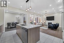 Kitchen featuring modern cabinets, light stone counters, light tile patterned floors, pendant lighting, and a kitchen island with sink - 