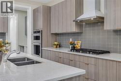 Kitchen featuring wall chimney range hood, light stone countertops, backsplash, and modern cabinets - 