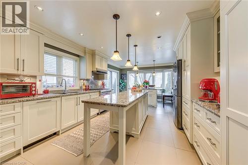 Kitchen featuring light stone counters, decorative light fixtures, light tile patterned flooring, stainless steel appliances, and crown molding - 4220 Millcroft Park Drive, Burlington, ON - Indoor Photo Showing Kitchen With Upgraded Kitchen
