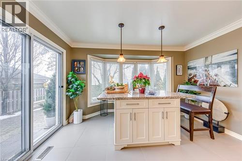 Kitchen with light stone countertops, hanging light fixtures, ornamental molding, a center island, and white cabinetry - 4220 Millcroft Park Drive, Burlington, ON - Indoor