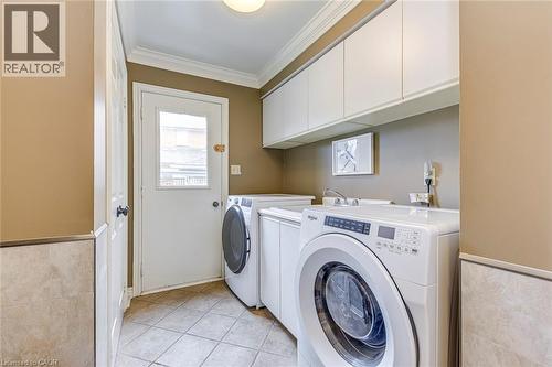Laundry area featuring a wainscoted wall, crown molding, cabinet space, light tile patterned floors, and washing machine and clothes dryer - 4220 Millcroft Park Drive, Burlington, ON - Indoor Photo Showing Laundry Room