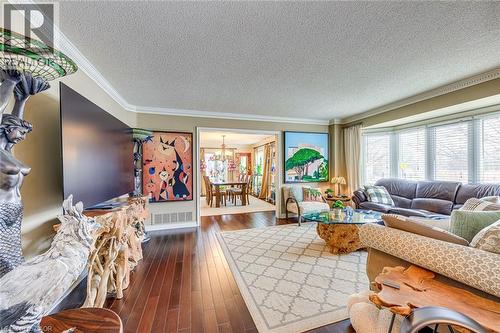 Living area featuring dark wood-type flooring, a textured ceiling, a chandelier, ornamental molding, and healthy amount of natural light - 4220 Millcroft Park Drive, Burlington, ON - Indoor Photo Showing Living Room