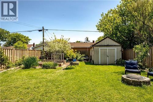 Expansive green lawn featuring a dedicated garden area with raised beds, a detached storage shed, privacy fencing, and a built-in stone fire pit - 364 Tragina Avenue N, Hamilton, ON - Outdoor With Backyard