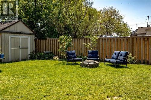 Spacious grass lawn featuring a stone fire pit, wood privacy fencing, and a detached storage shed with double doors - 364 Tragina Avenue N, Hamilton, ON - Outdoor With Backyard