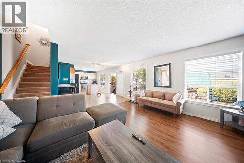 Living room with stairs, a textured ceiling, dark wood-type flooring, and a chandelier - 132 Blackburn Drive, Brantford, ON - Indoor Photo Showing Living Room
